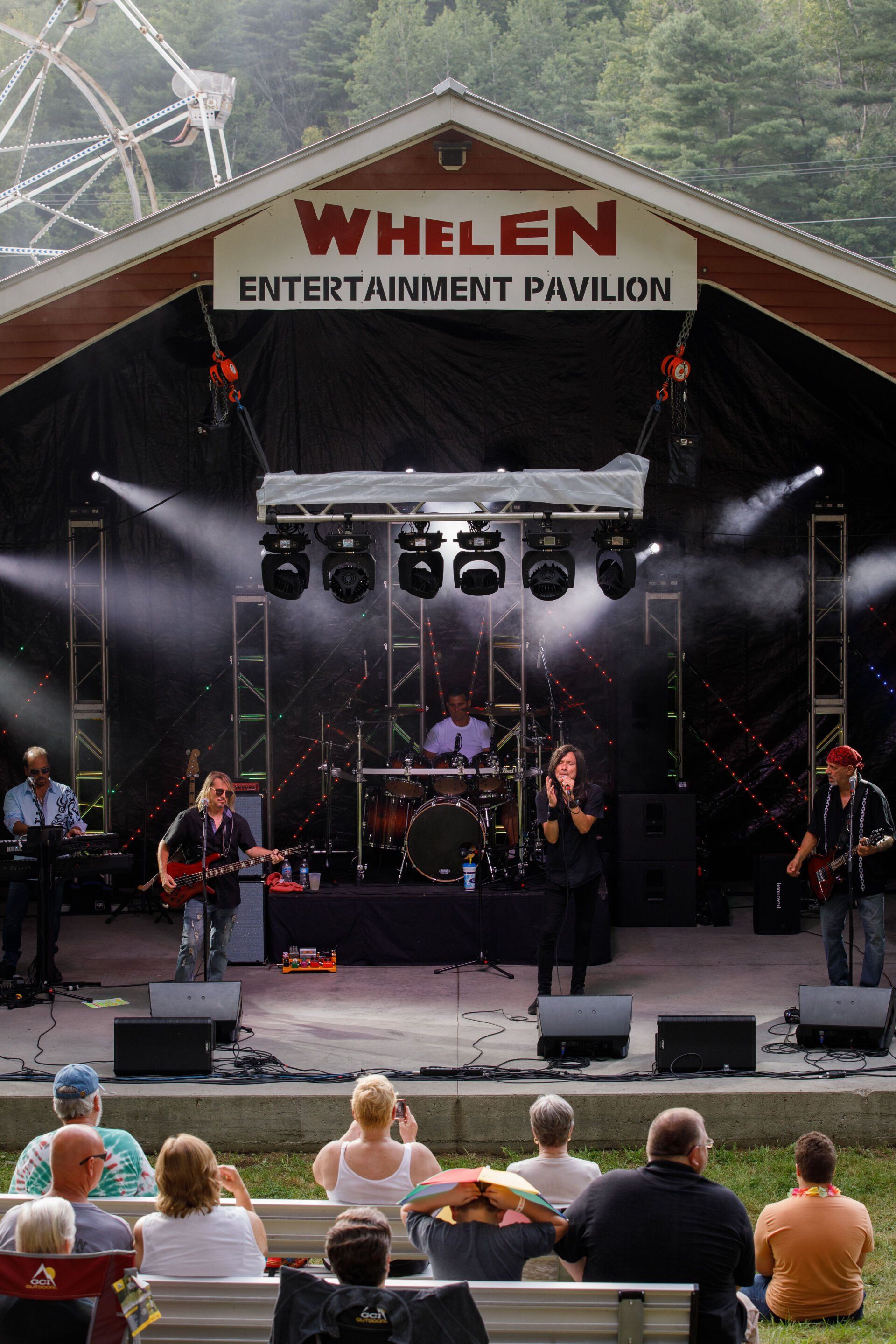A group of people are watching a band on stage at the whelen entertainment pavilion