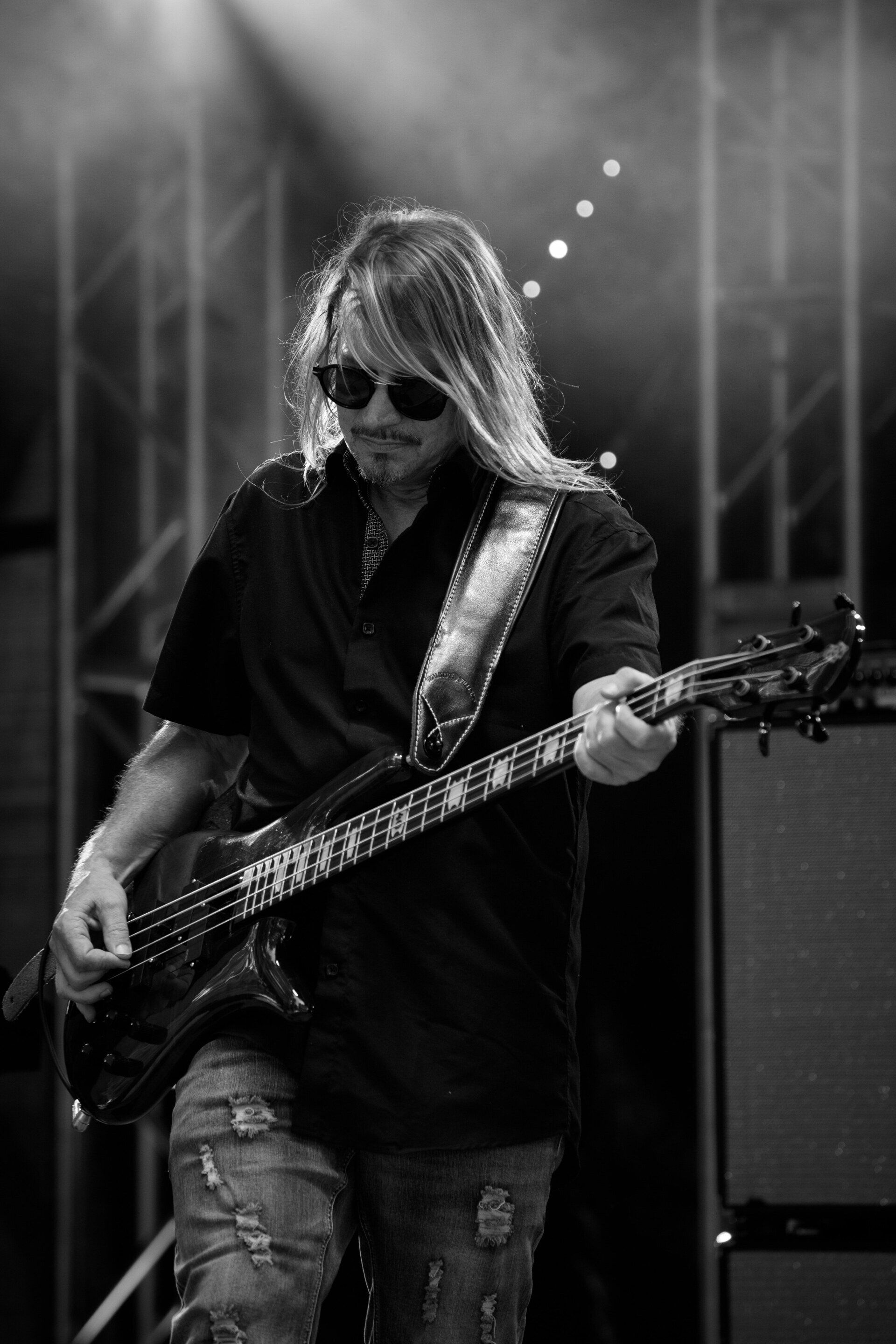 A man is playing a bass guitar on stage in a black and white photo.