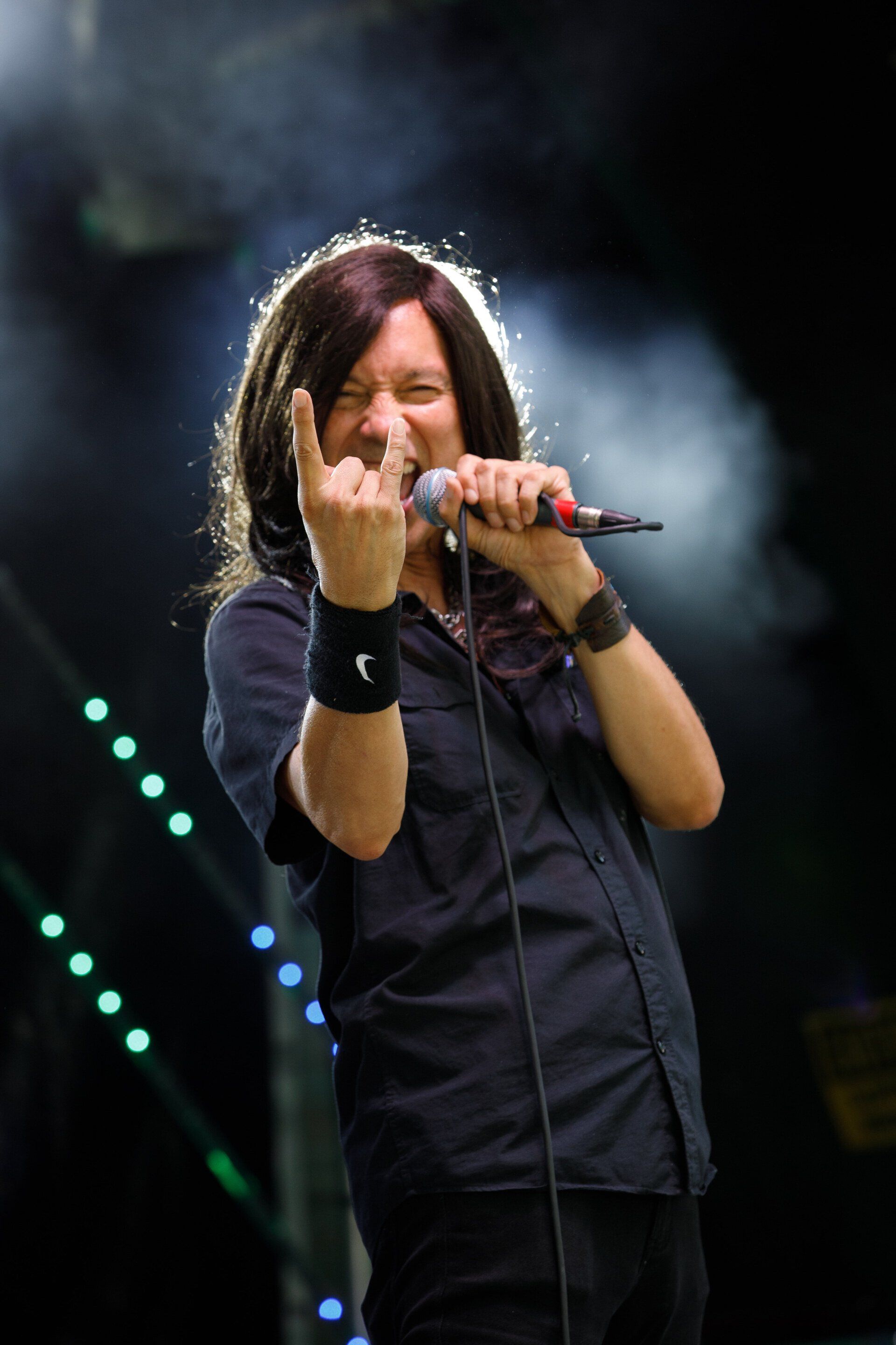 A man with long hair is singing into a microphone and making a devil horns sign.