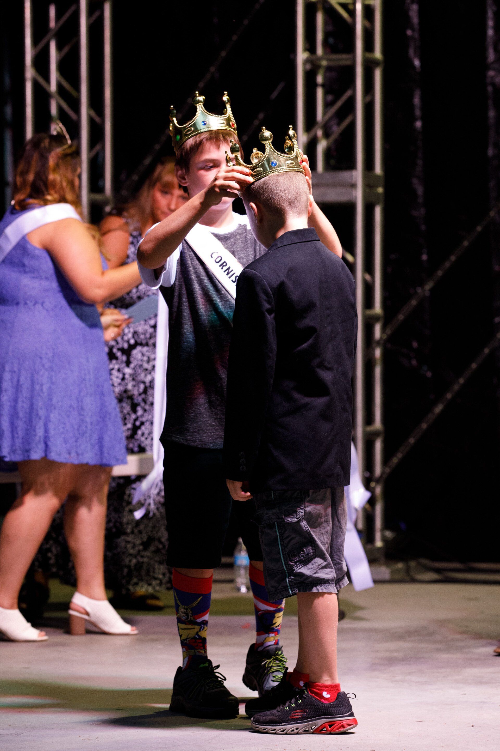 Two boys wearing crowns are standing on a stage