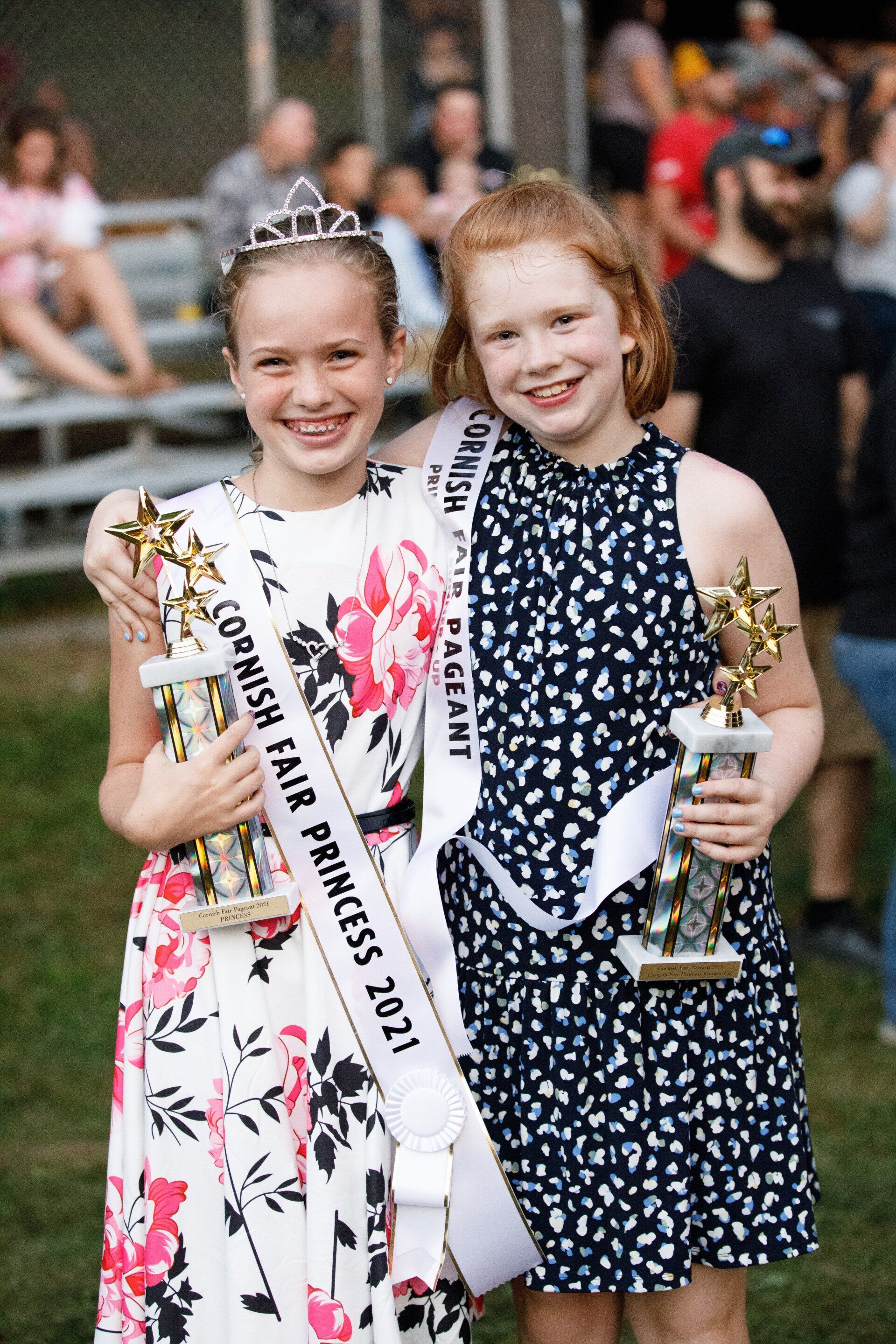 Two young girls are posing for a picture while holding trophies.