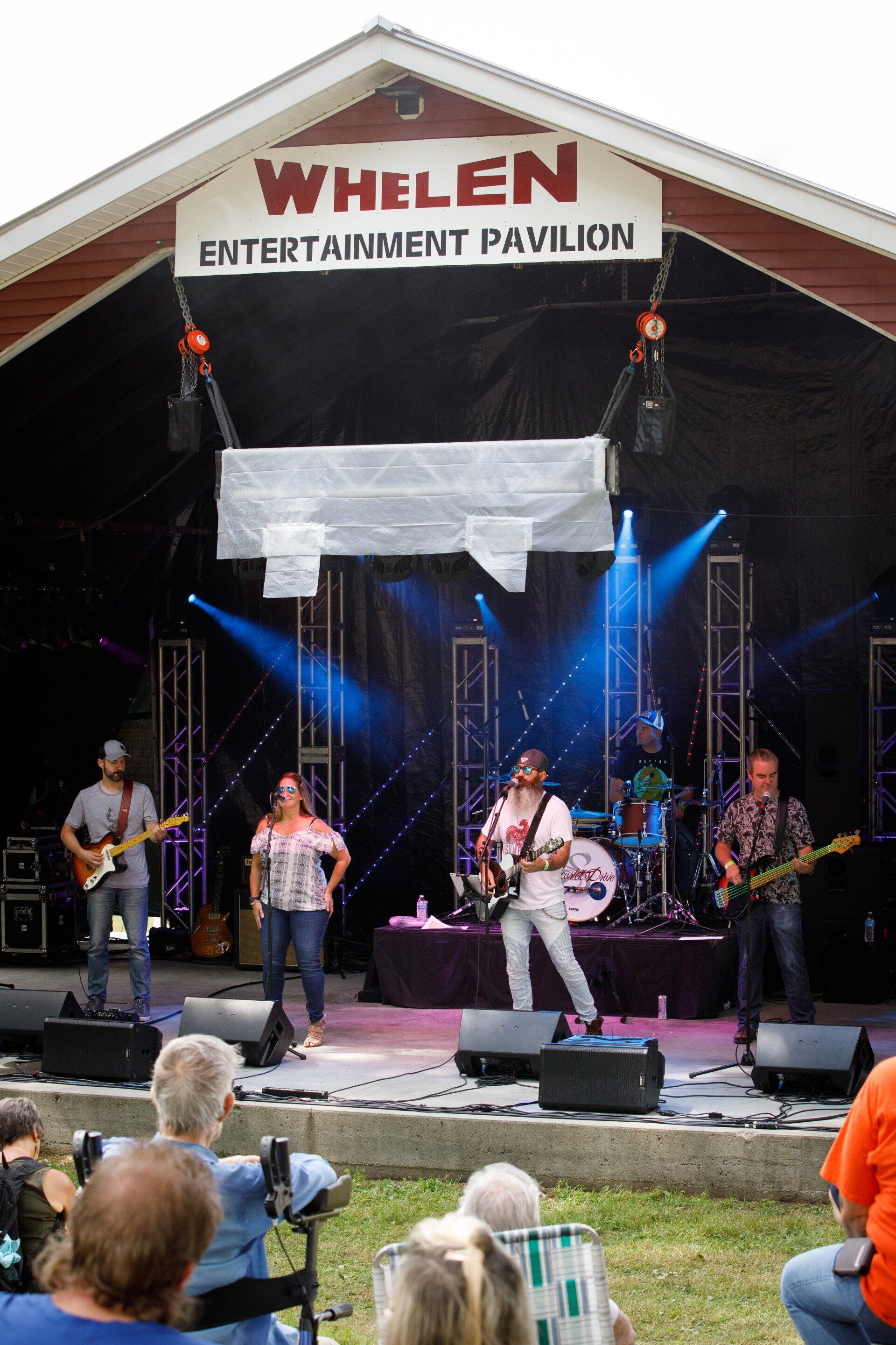 A group of people are sitting in chairs watching a band perform on a stage.
