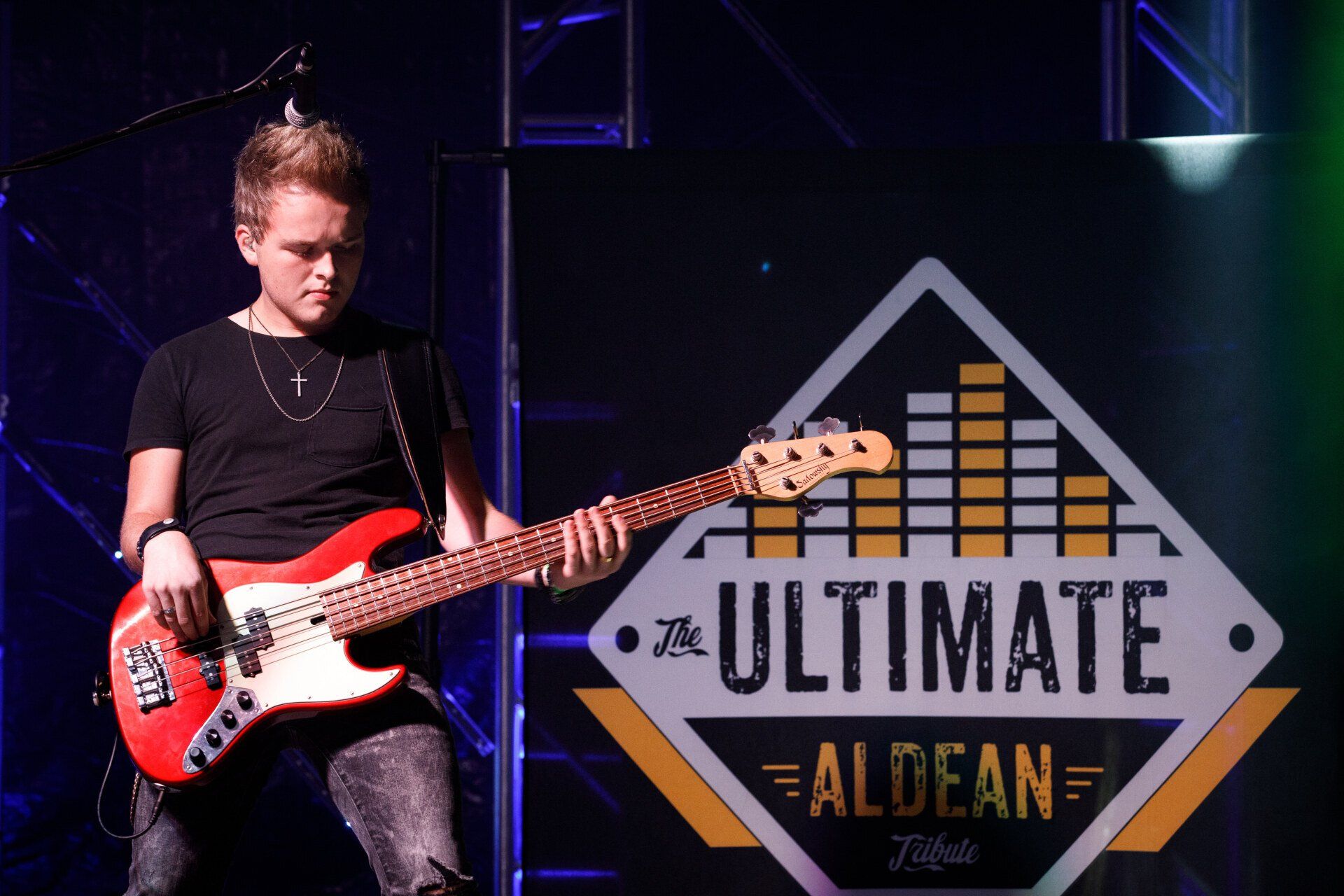 A man is playing a red guitar in front of a sign that says ultimate