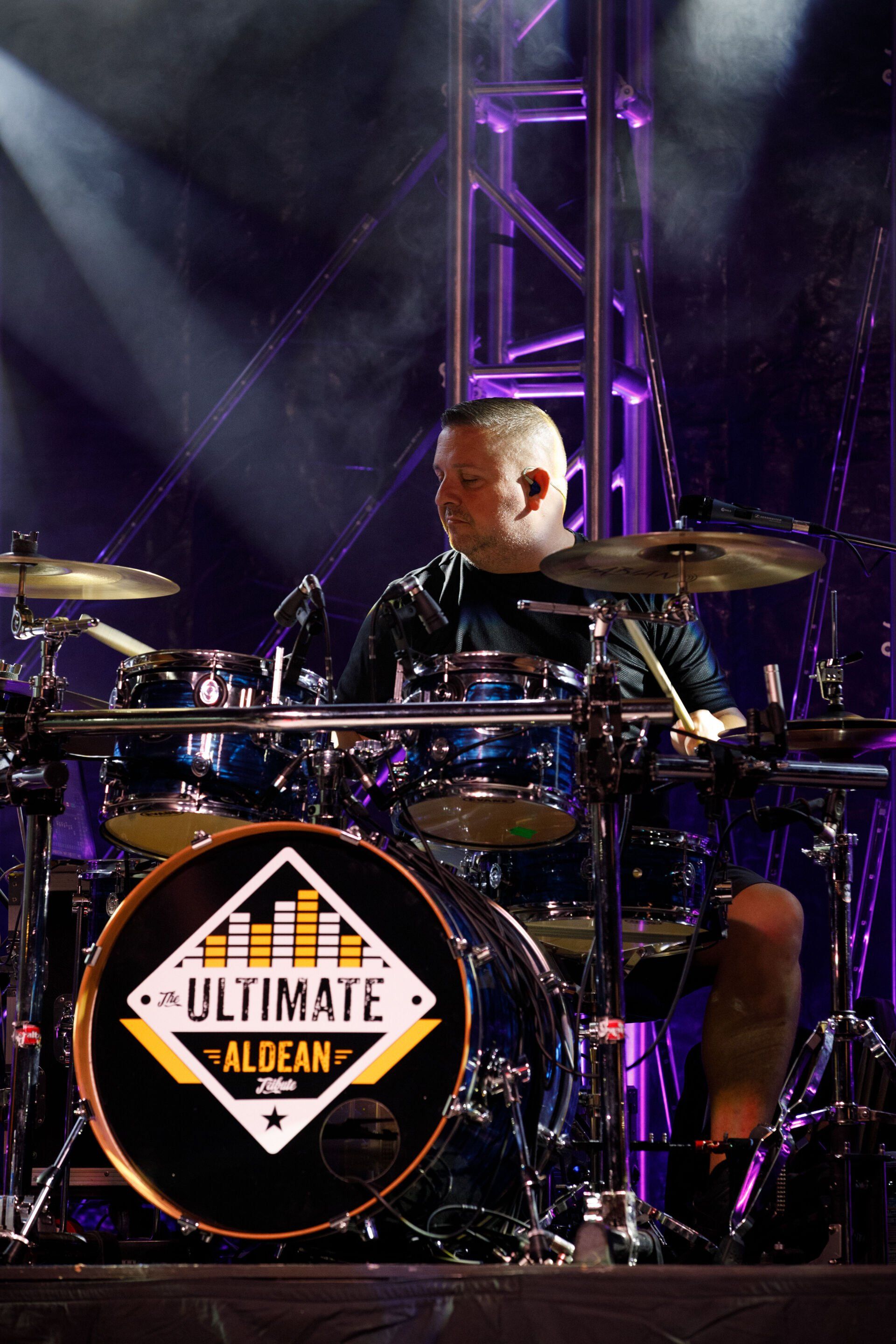 A man is playing drums in front of a drum set that says ultimate