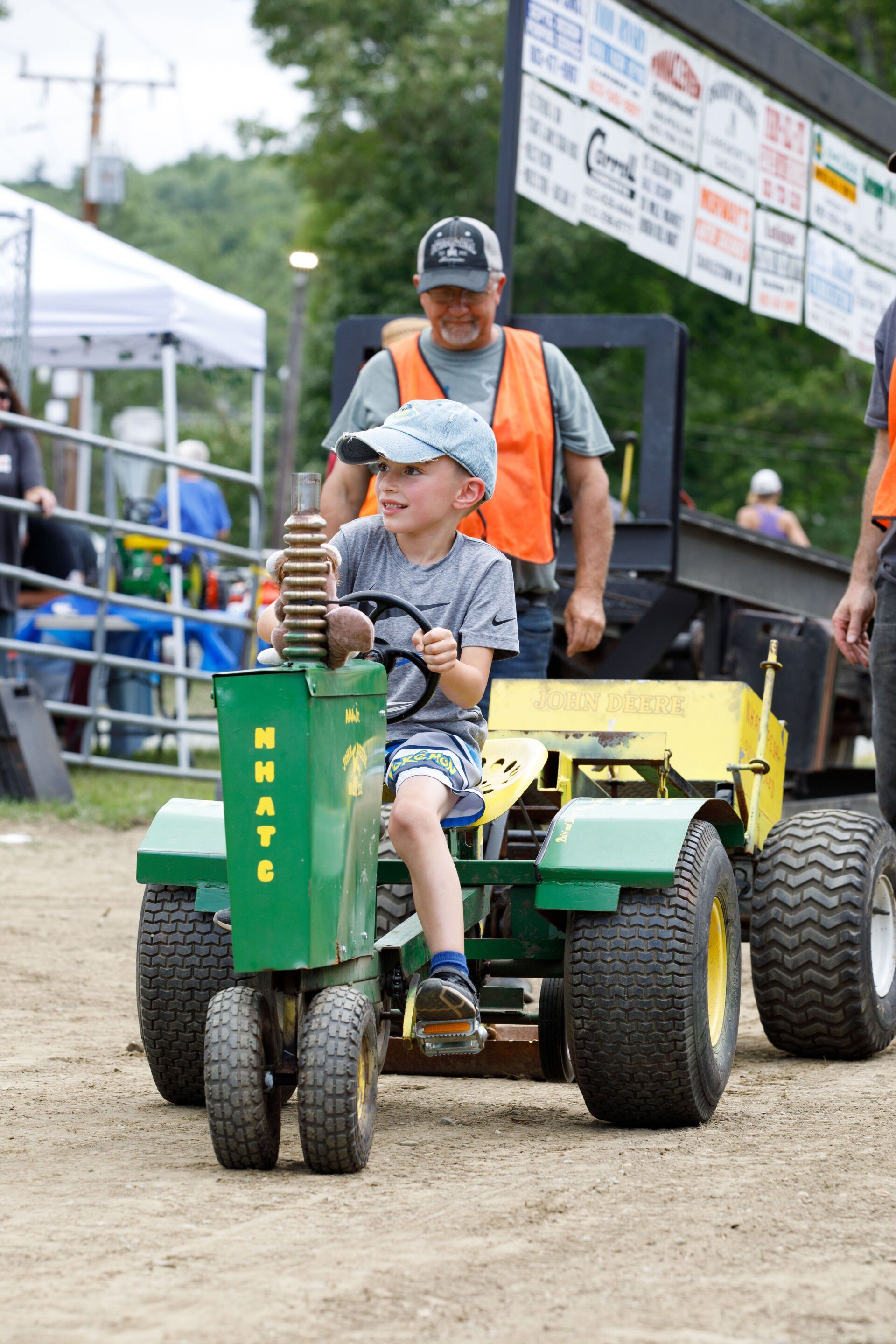 A young boy is riding a john deere lawn mower on a dirt road.
