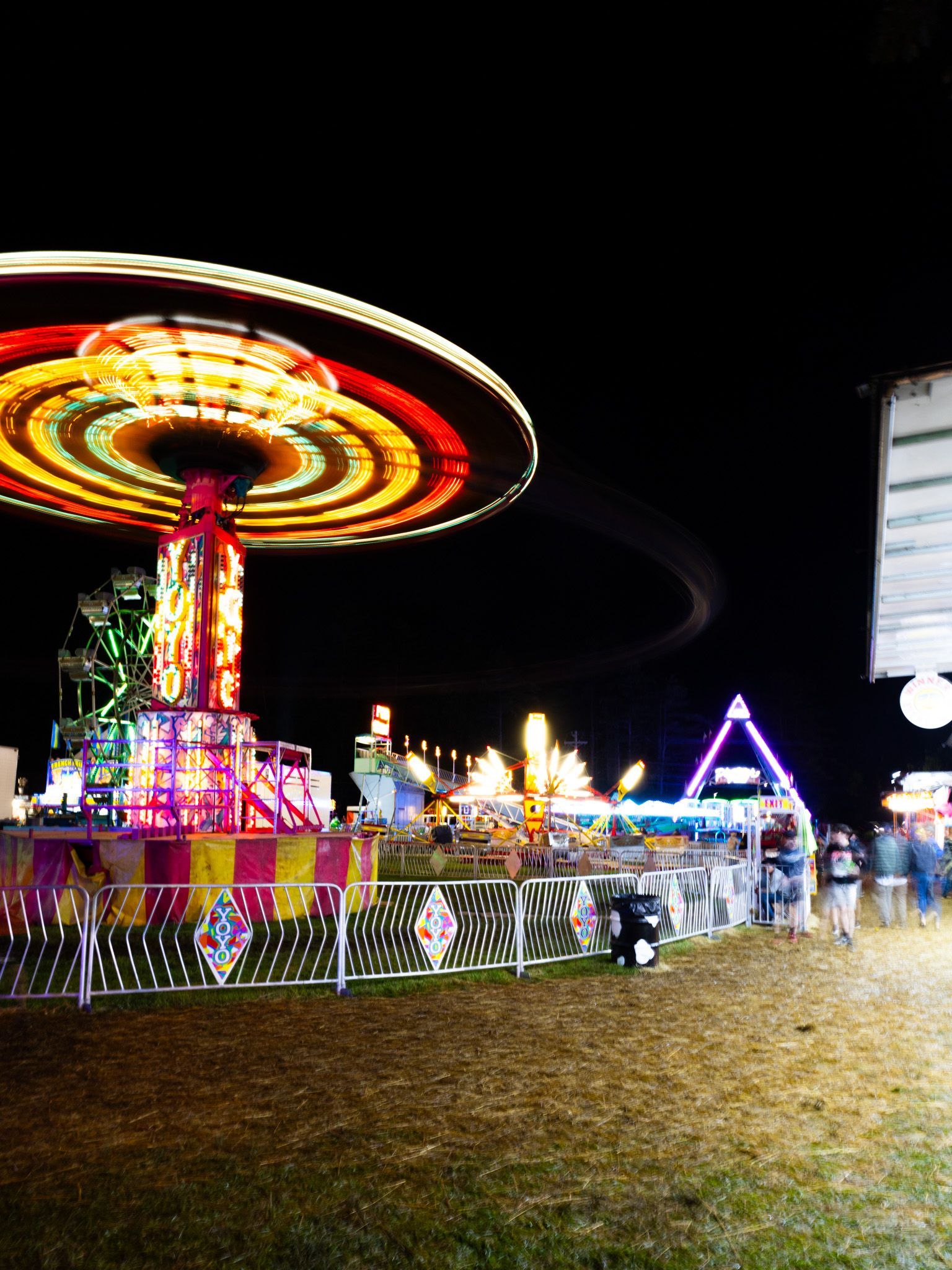 Night carnival ride with spinning lit canopy and colorful booths at dusk