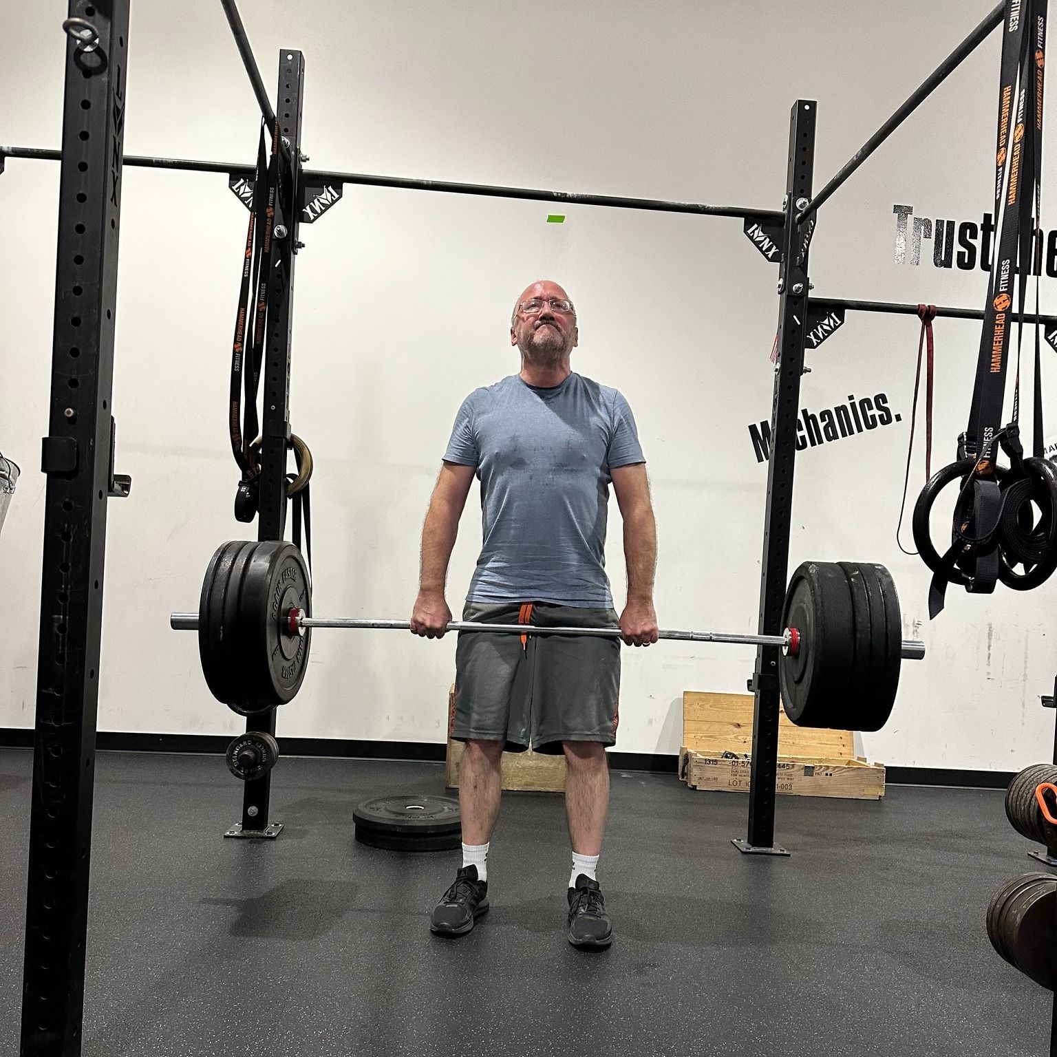 People exercising with weights at Mad Mare CrossFit gym in Alpharetta, GA. Some seated, some standing. A coach observes