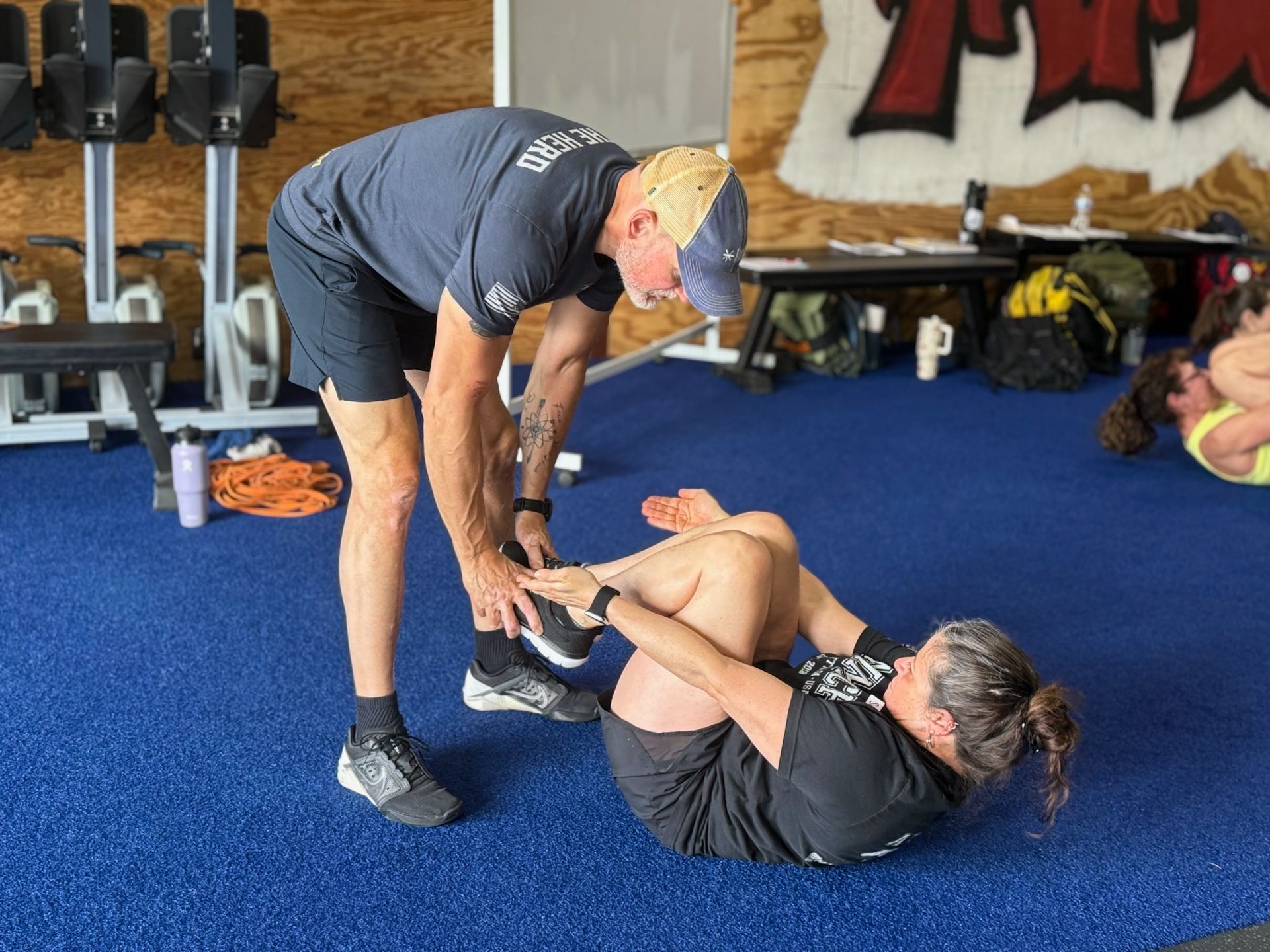 Trainer assisting person doing crunches on a blue floor at Mad Mare CrossFit gym in Alpharetta, GA.