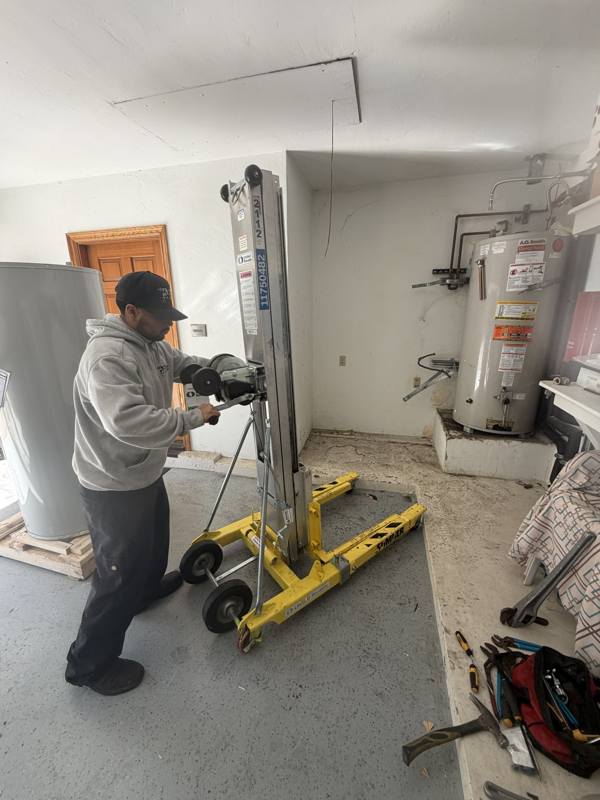 Person using a yellow hand truck to move a tall ladder in a small unfinished room.
