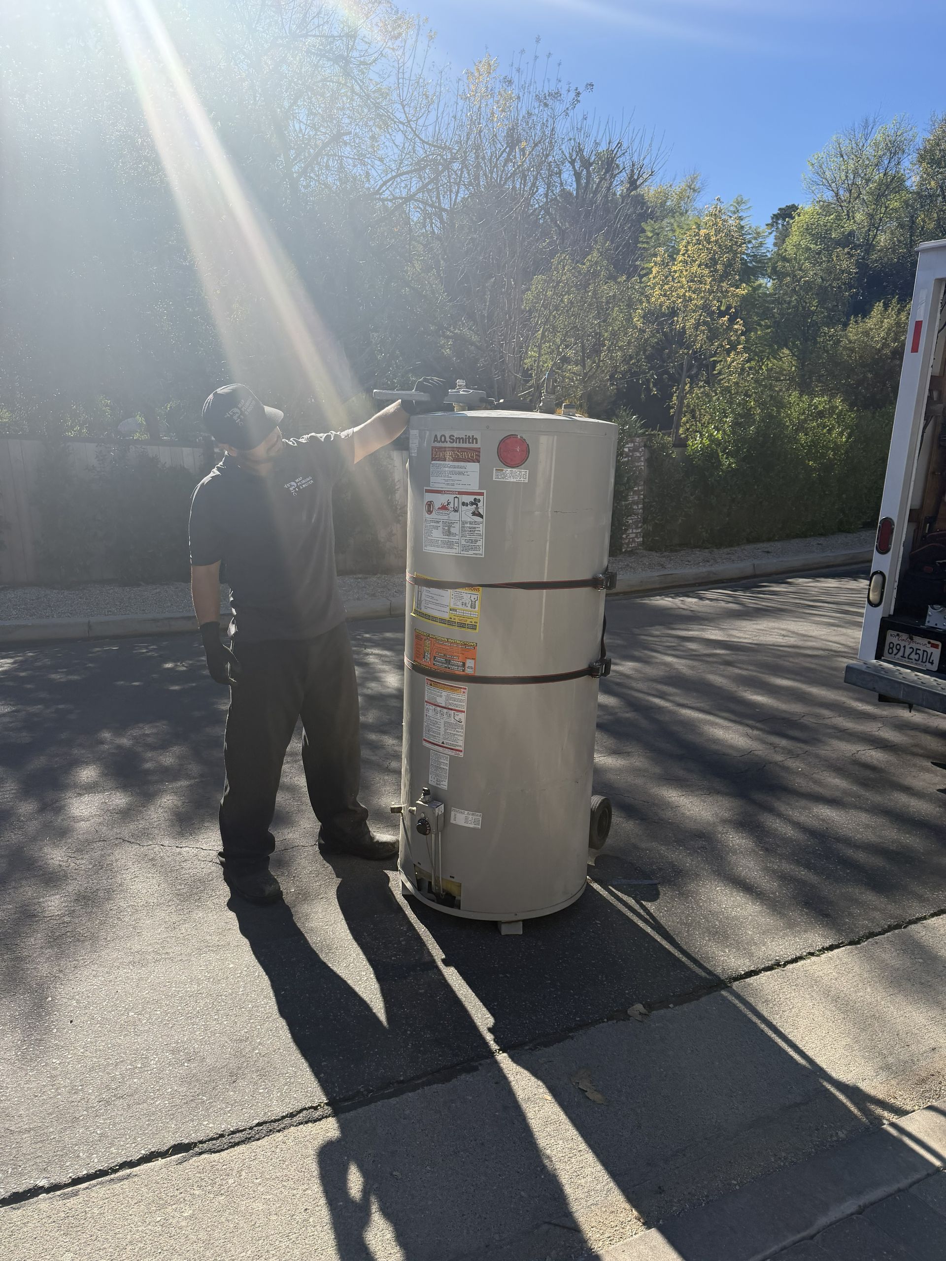 Person standing beside two white propane tanks on a sunny driveway