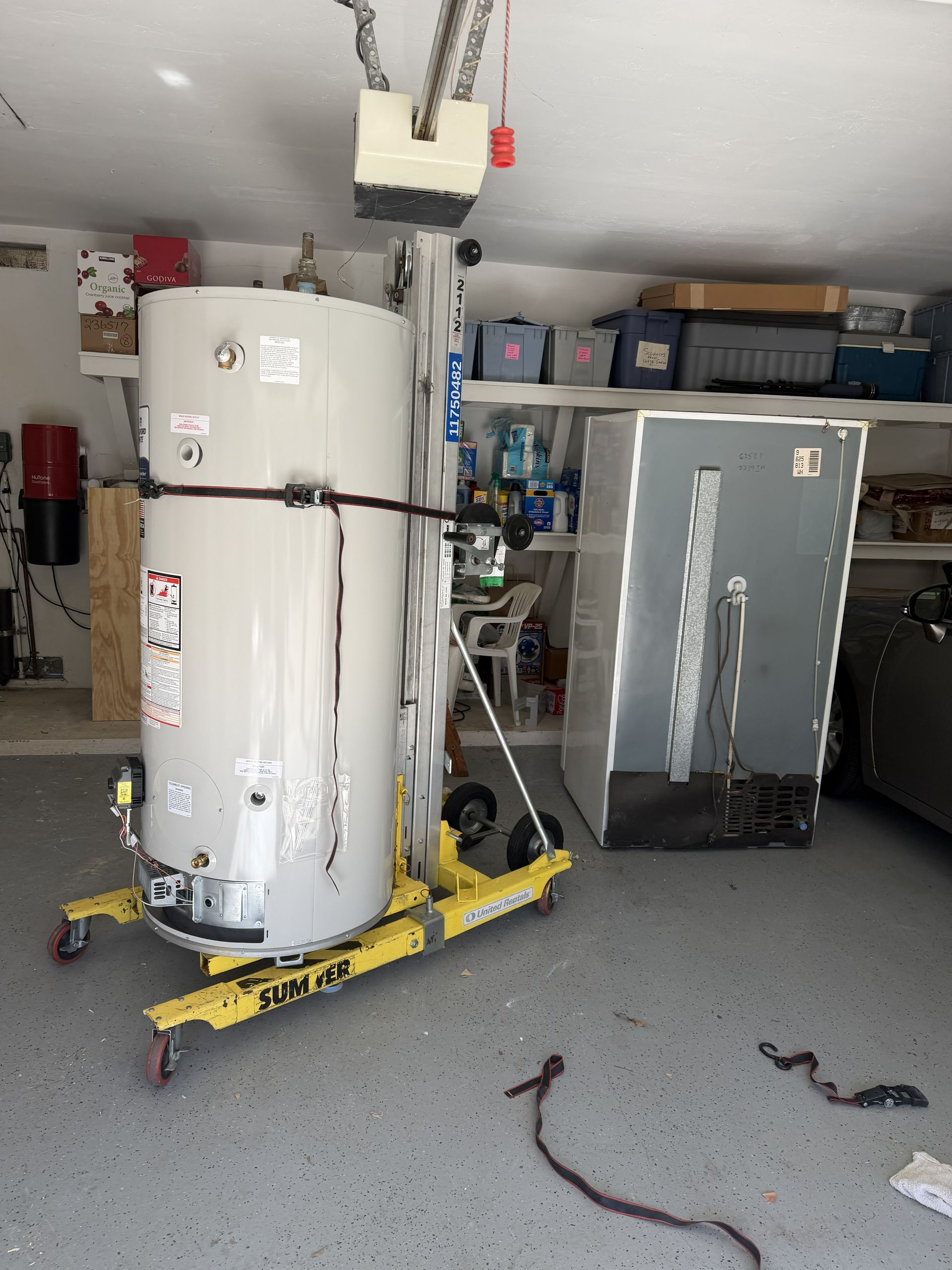 Garage with a water heater and HVAC unit on dollies, strapped for installation or moving.