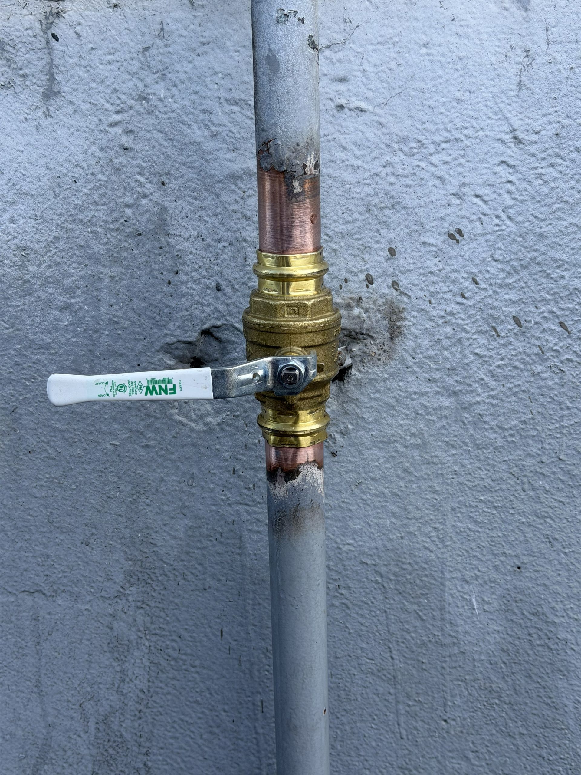 Close-up of a copper pipe repair with a brass valve against a gray wall