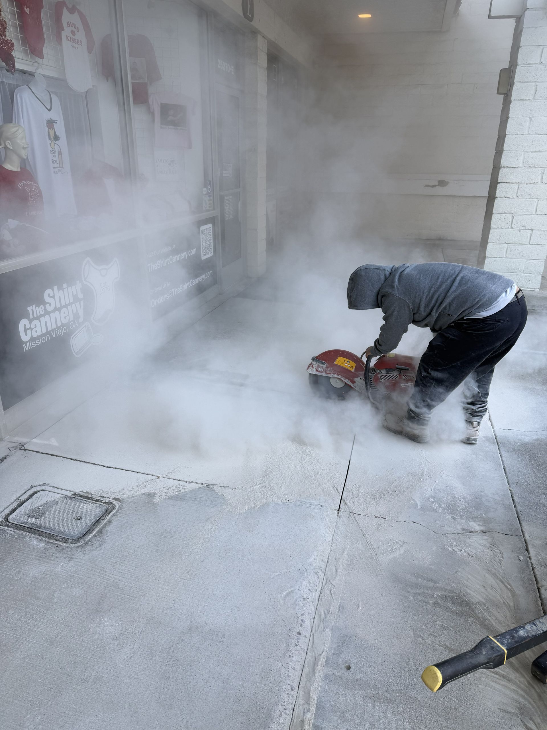 Worker using a concrete saw amid heavy dust outside a building entrance