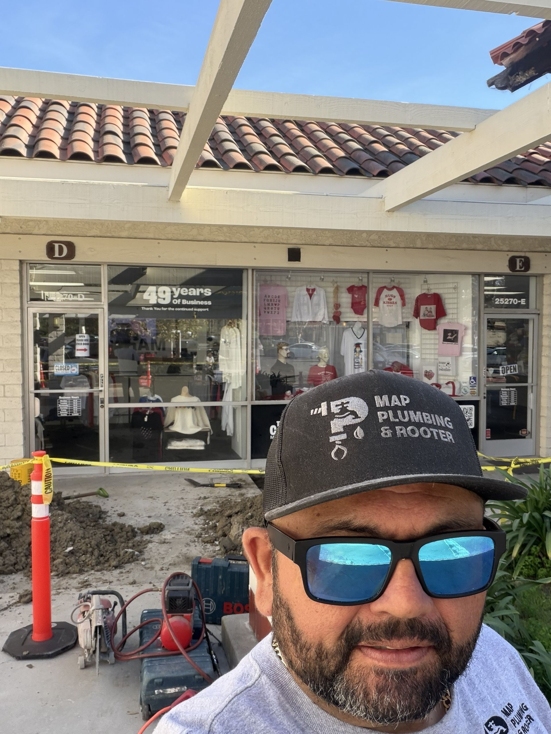 Man in sunglasses and black cap taking a selfie outside a storefront under construction with tools and scaffolding