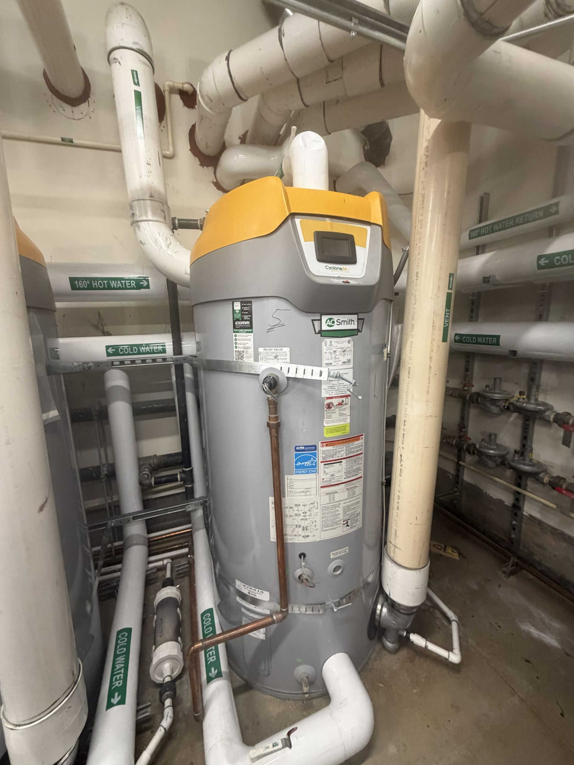 Residential water heater in a utility closet with exposed pipes and ventilation lines.