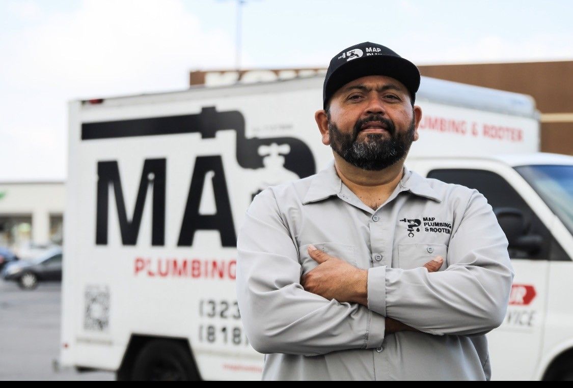 Man standing arms crossed in front of a plumbing service van and truck sign