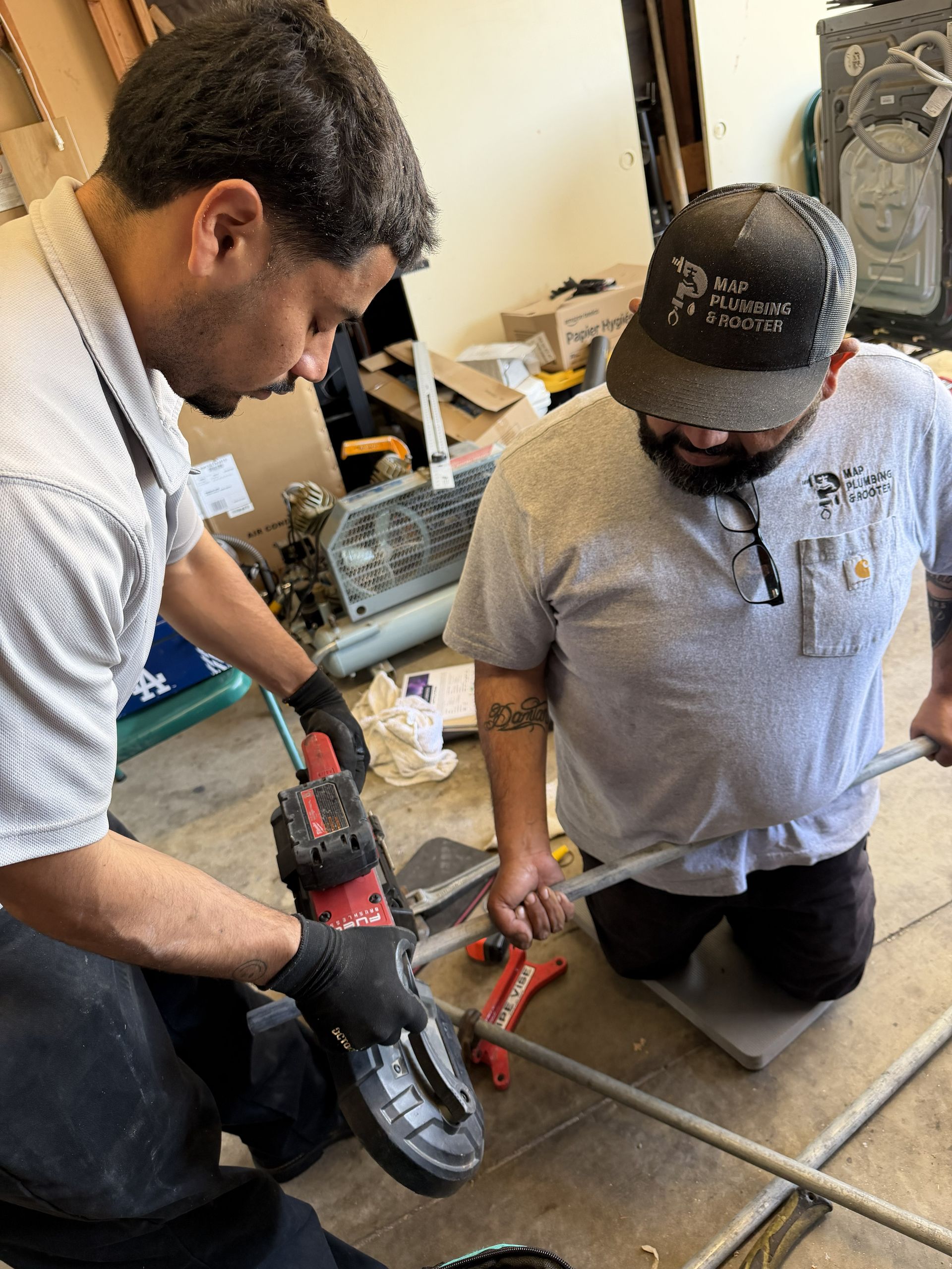 Two workers using power tools to cut metal pipe on a workshop floor