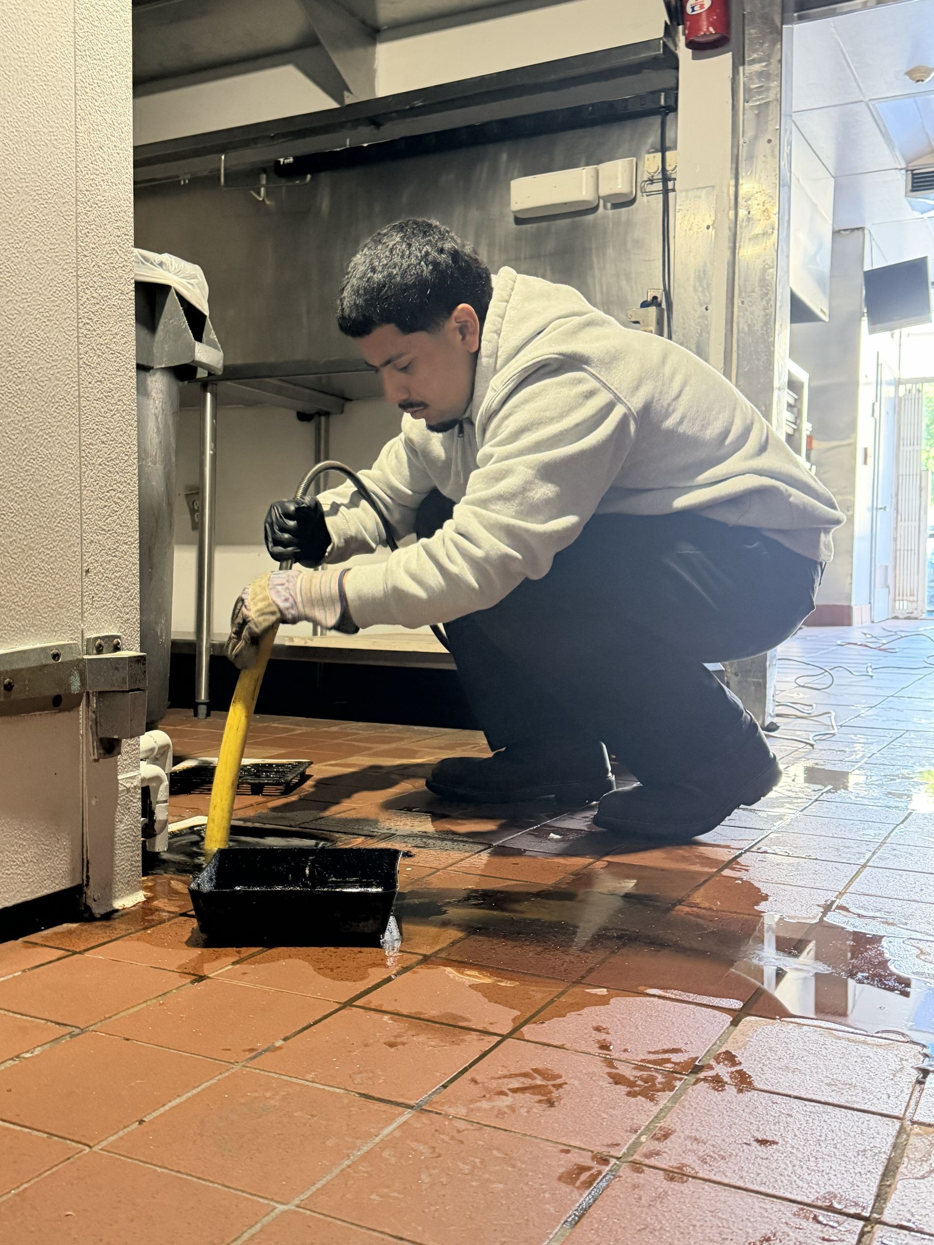 Person crouches mopping a wet tiled floor in a commercial kitchen.