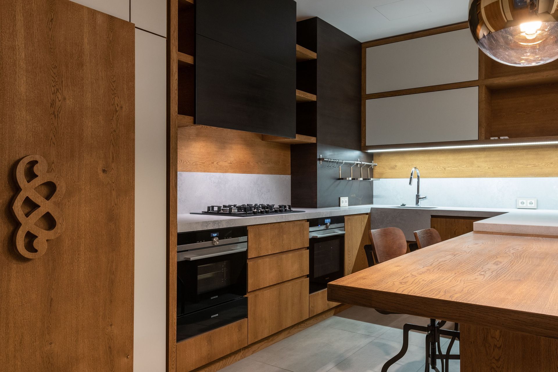 Modern kitchen with wood cabinets, black appliances, and a large wooden island under warm lighting