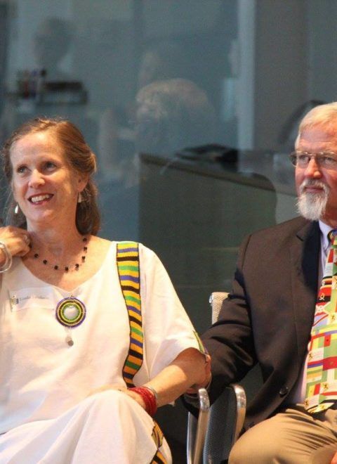 Two people seated indoors, smiling during a meeting or event.
