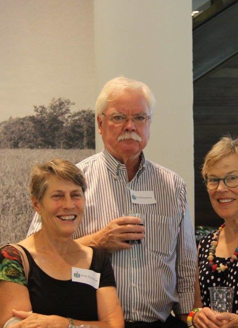 Three people standing indoors, smiling at a gathering, wearing name tags.
