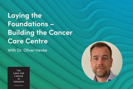 Promo slide with teal waves, a man’s headshot, and text: “Laying the Foundations – Building a Cancer Care Centre”