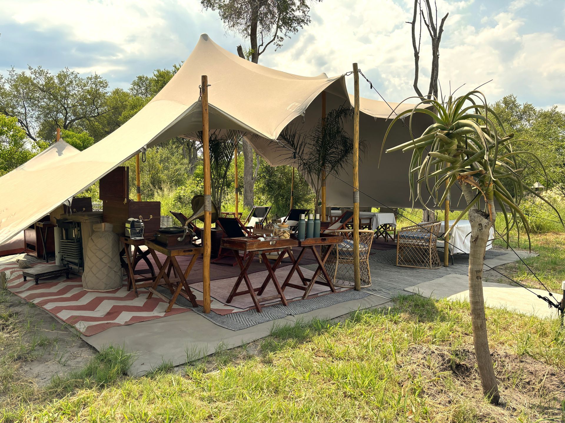 Outdoor café under beige tents with wooden tables and chairs on a grassy patio.