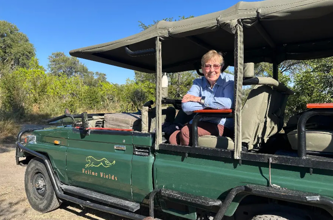 Green safari vehicle with an open roof, parked outdoors, with a person seated inside and smiling.