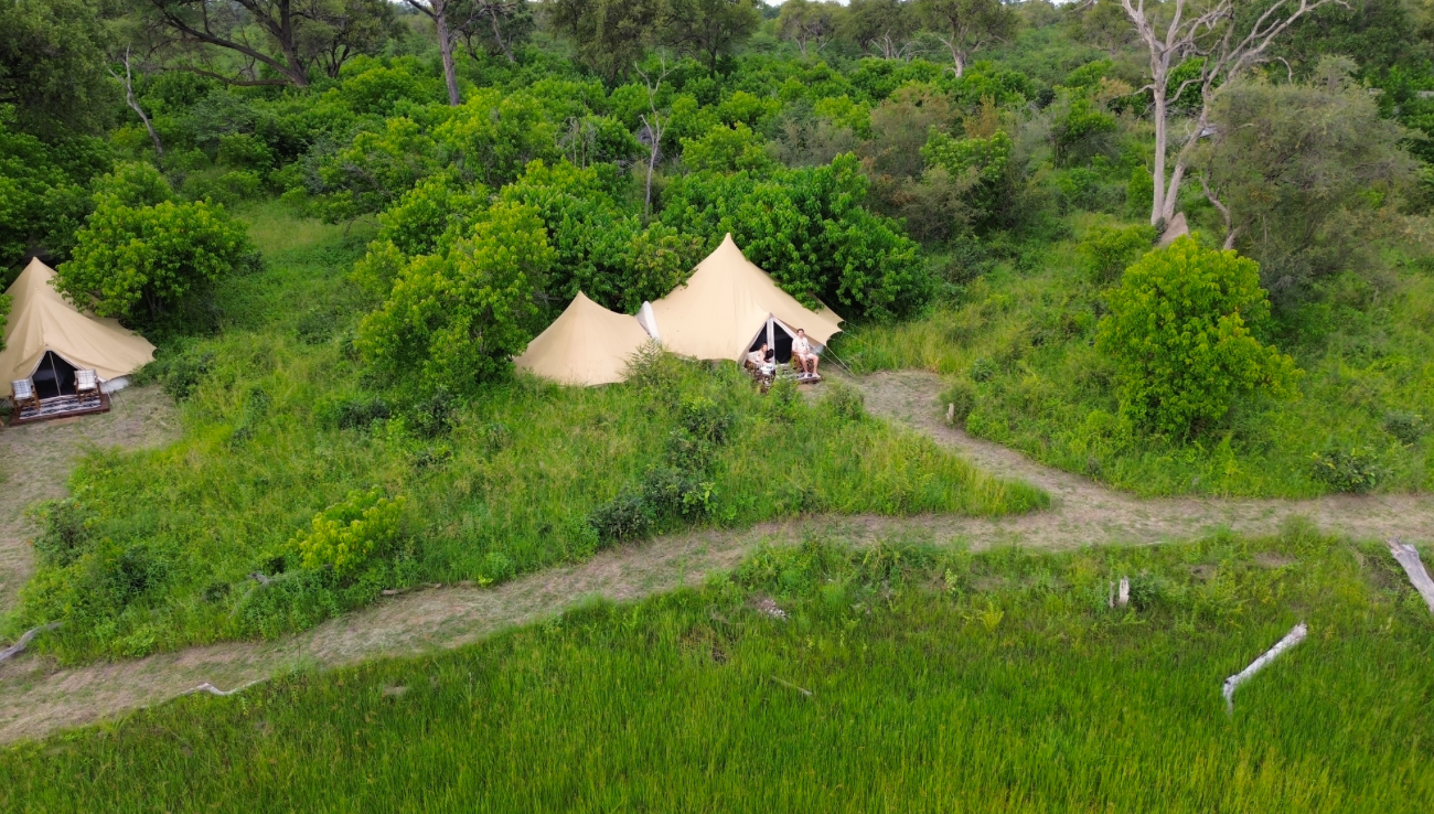 Small beige tents on a green bank of the Mbudi Channel beside a narrow path