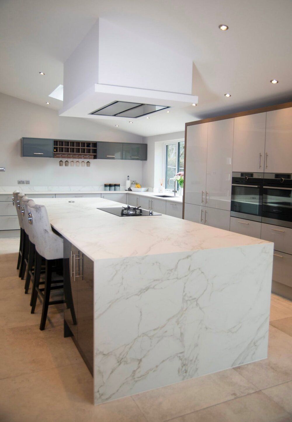 Modern white kitchen with a large marble island, black stools, and built-in appliances