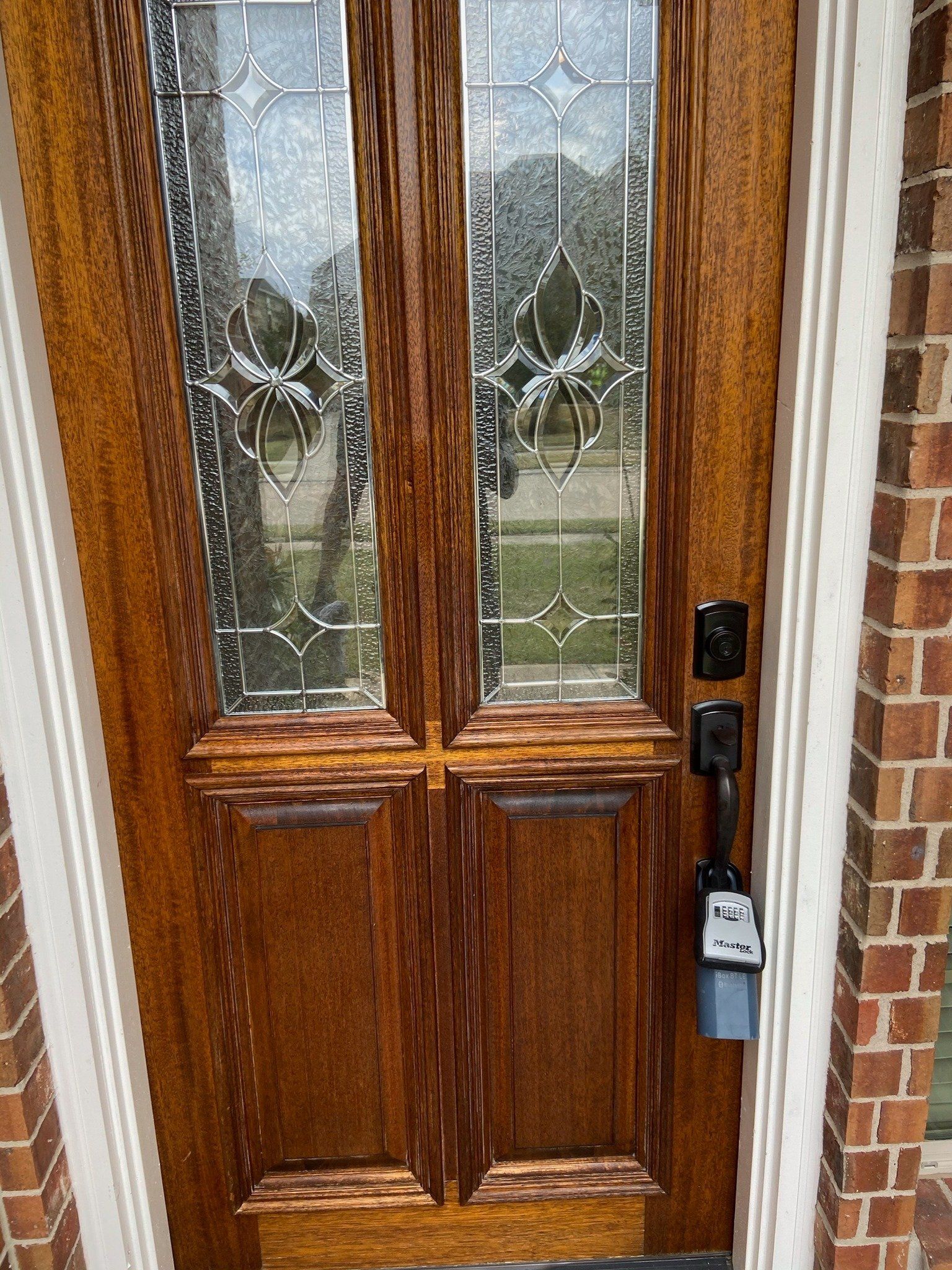Wooden front door with textured glass panes and a lockbox hanging on the handle.