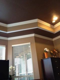 Brown room with white crown molding, a window with blinds, and a dark dresser under a ceiling light