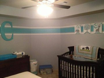 Nursery room with teal wall border, crib, dresser, and ceiling fan under a bright light