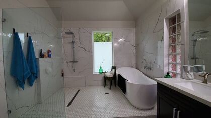 Bright white bathroom with glass shower, freestanding tub, and sink vanity by a window.