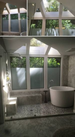 Bright bathroom with frosted windows, skylight, white tub, and gray tile floor