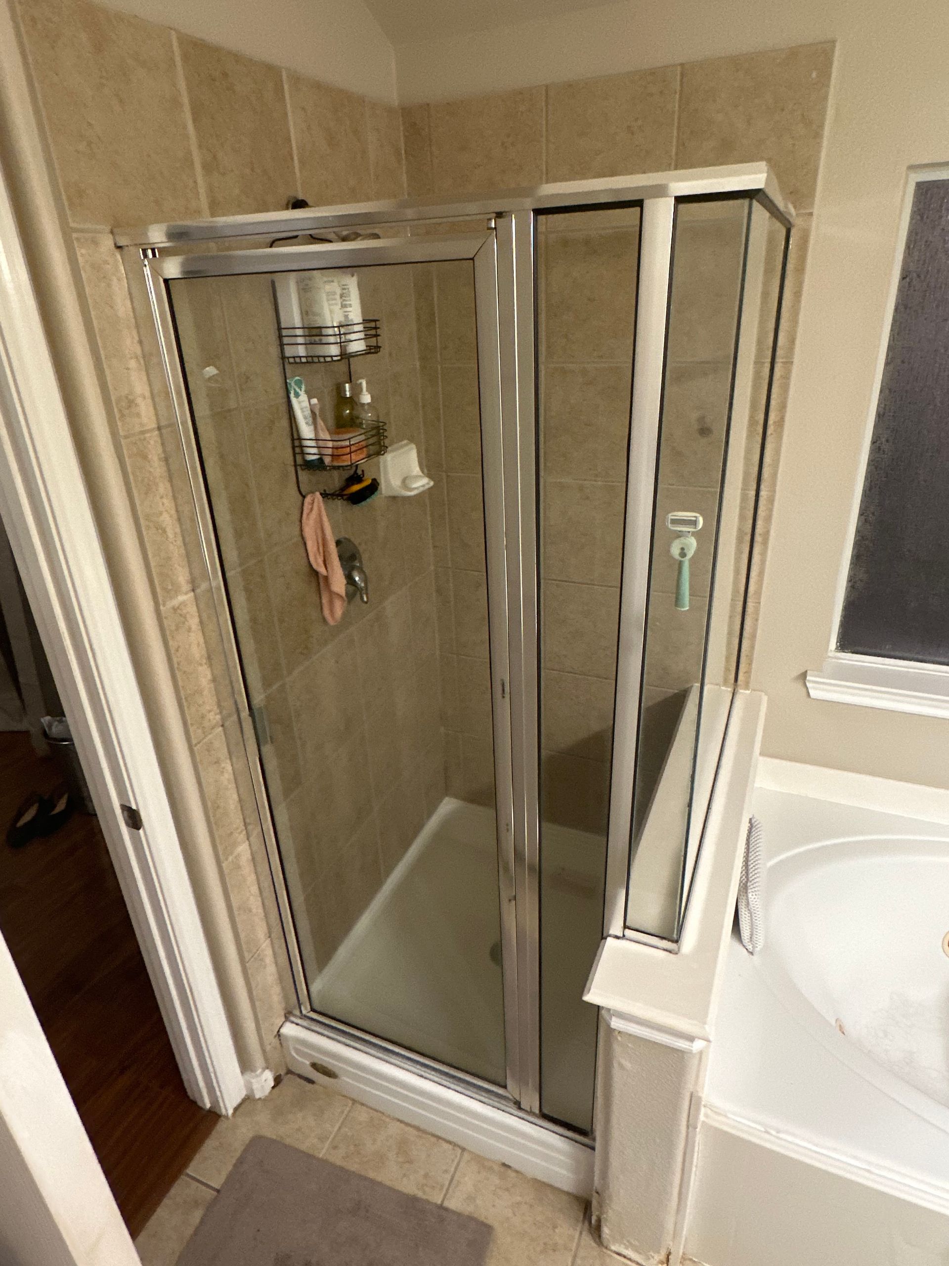 Bathroom shower stall with glass doors beside a bathtub, in a beige-tiled room.