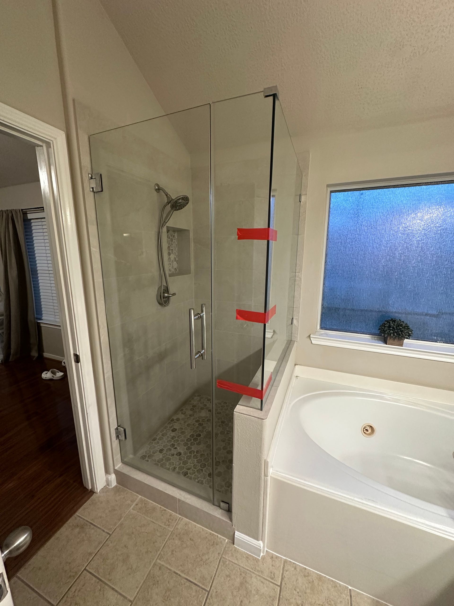 Bathroom with glass shower enclosure, white bathtub, and tiled floor, with red markers on the shower frame.