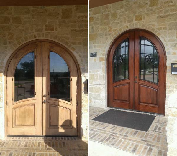 Two arched wooden double doors with glass panes in a stone exterior wall.