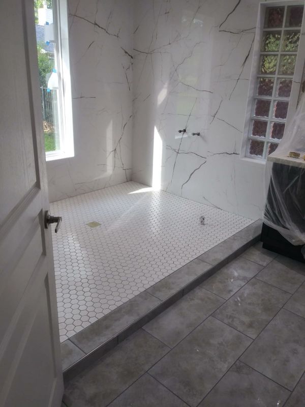 Small white-tiled shower or wet room with a bench and marble-patterned walls.