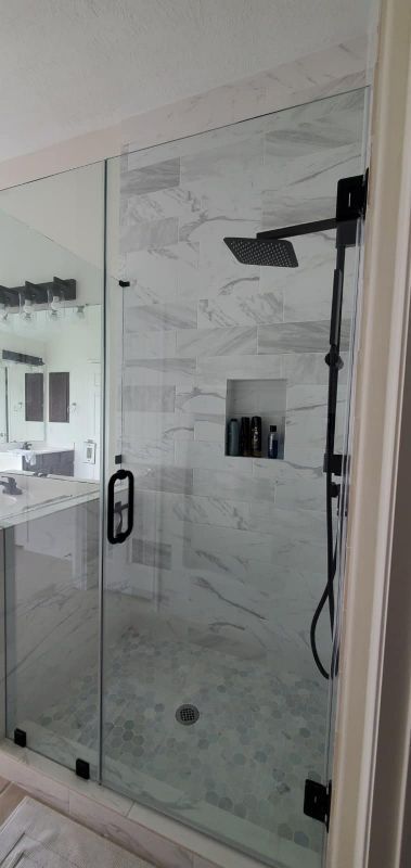 Glass shower enclosure with marble tile walls and a black shower fixture
