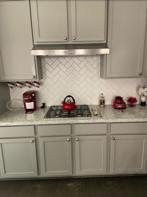 Red-accented kitchen with gray cabinets, white herringbone backsplash, and red appliances on the countertop