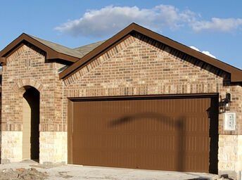 Brick suburban house with a brown garage door and stone trim under a clear sky