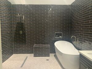 Modern bathroom with dark tiled walk-in shower, freestanding tub, and white vanity.