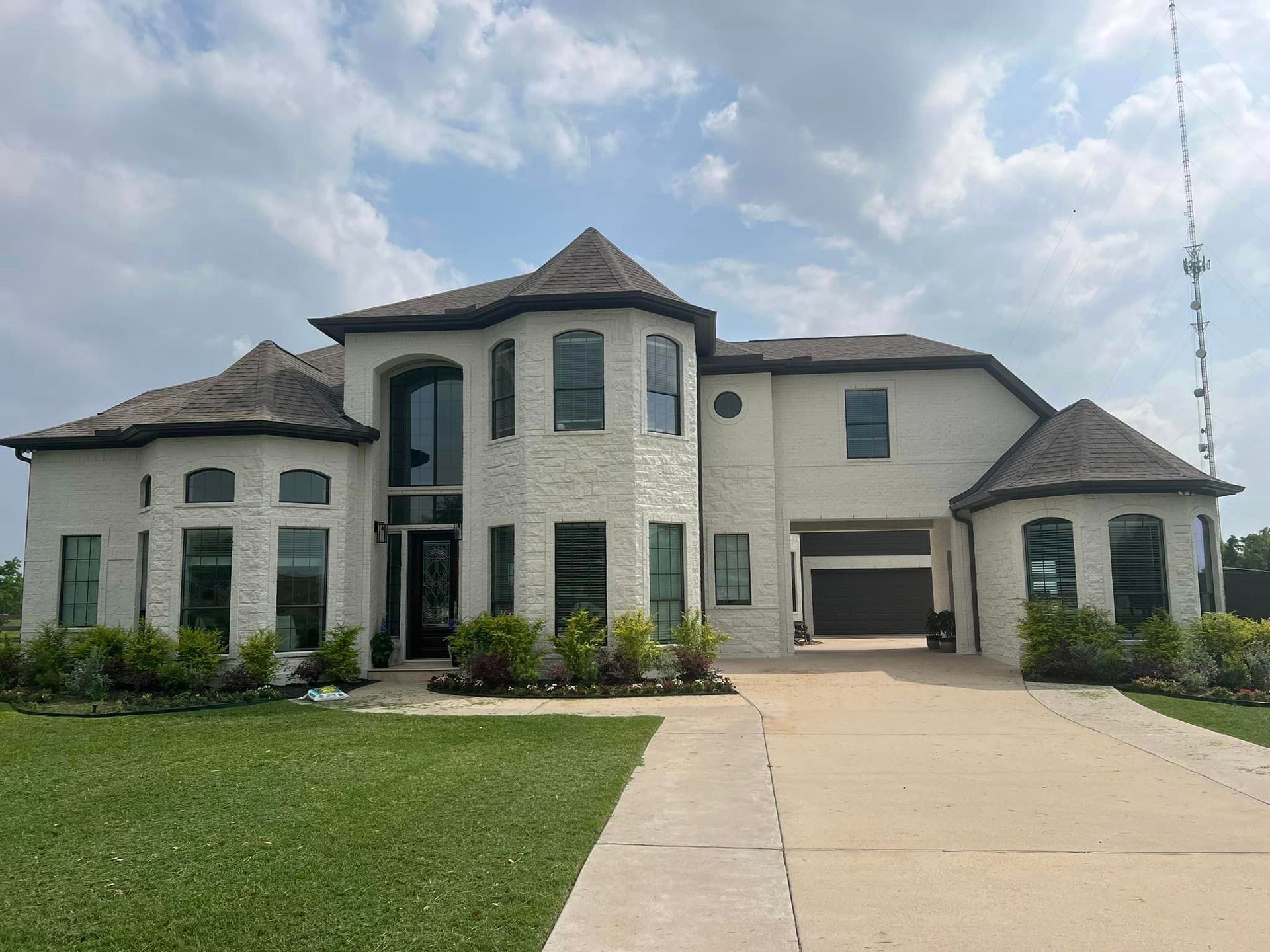 Large two-story modern house with white stone exterior, driveway, and green lawn under a cloudy sky