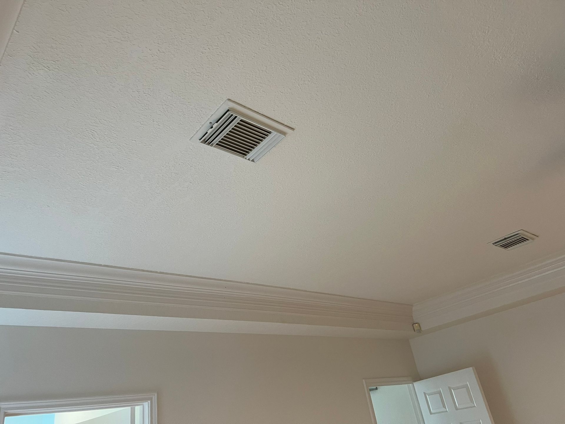 Ceiling with two vents, crown molding, and part of a window and door in a light-colored room