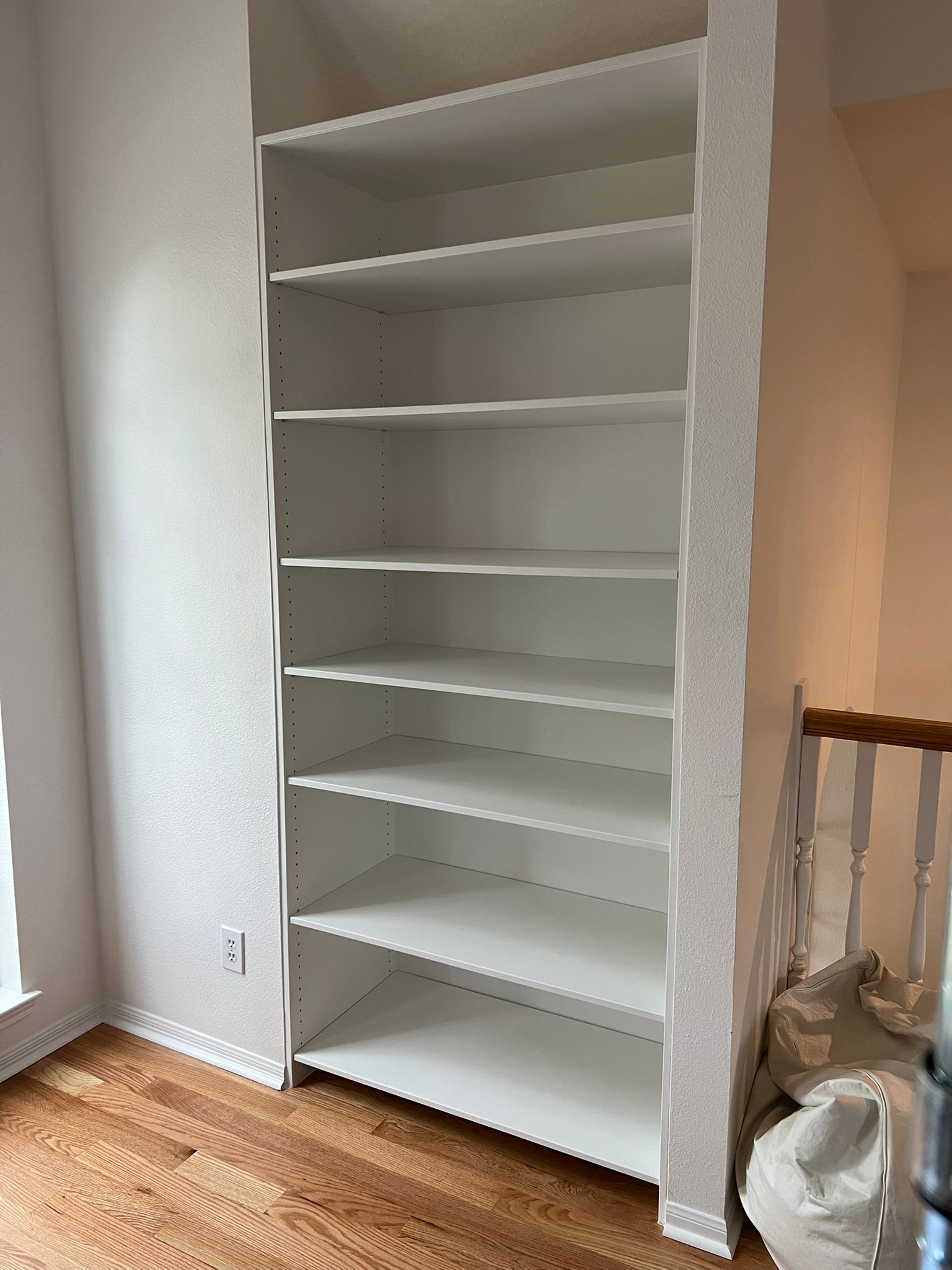 Empty white bookshelf in a room with wood floors and a window on the left.