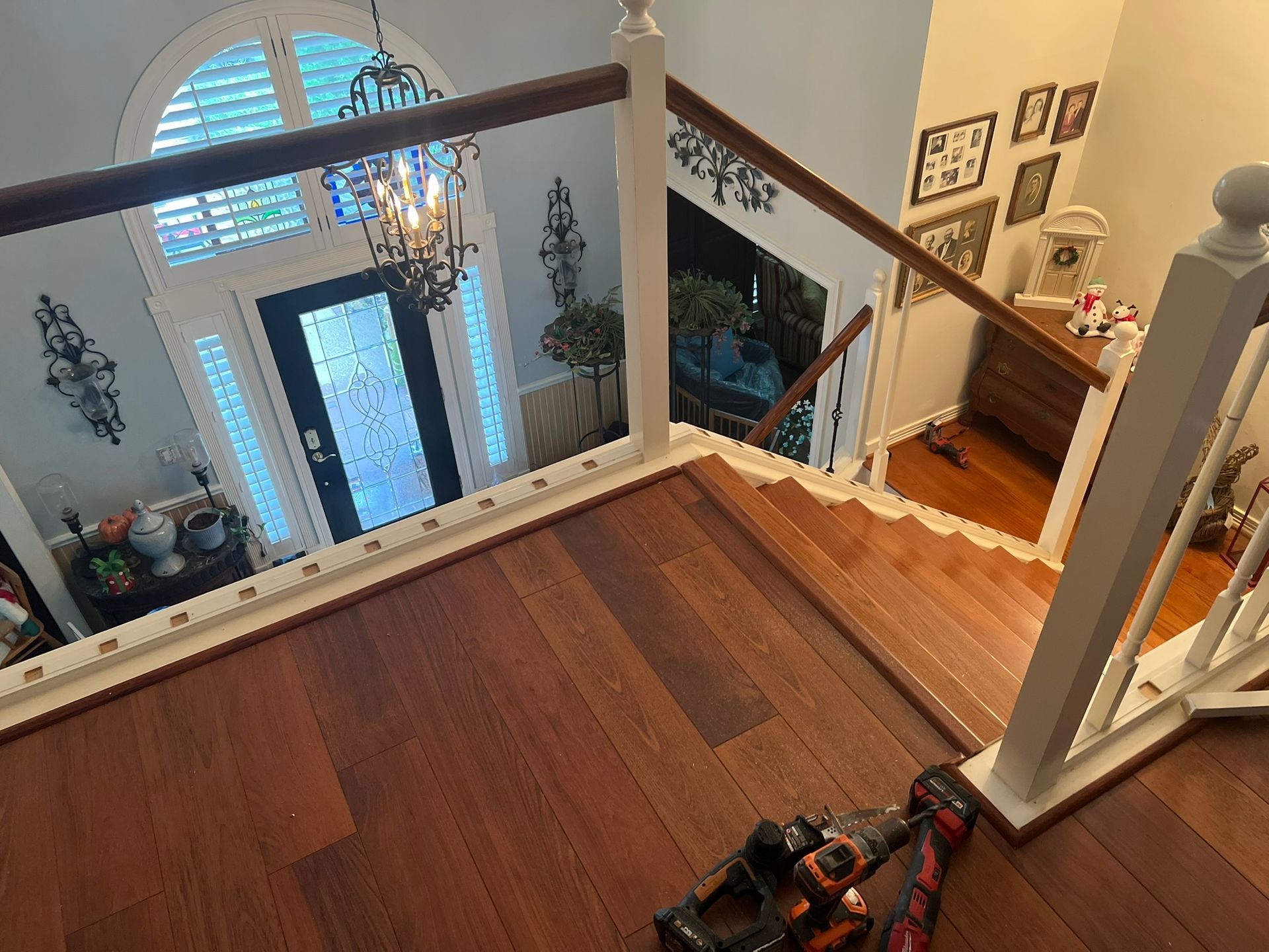 Top of a hardwood staircase overlooking a bright foyer with a front door, chandelier, and railing。