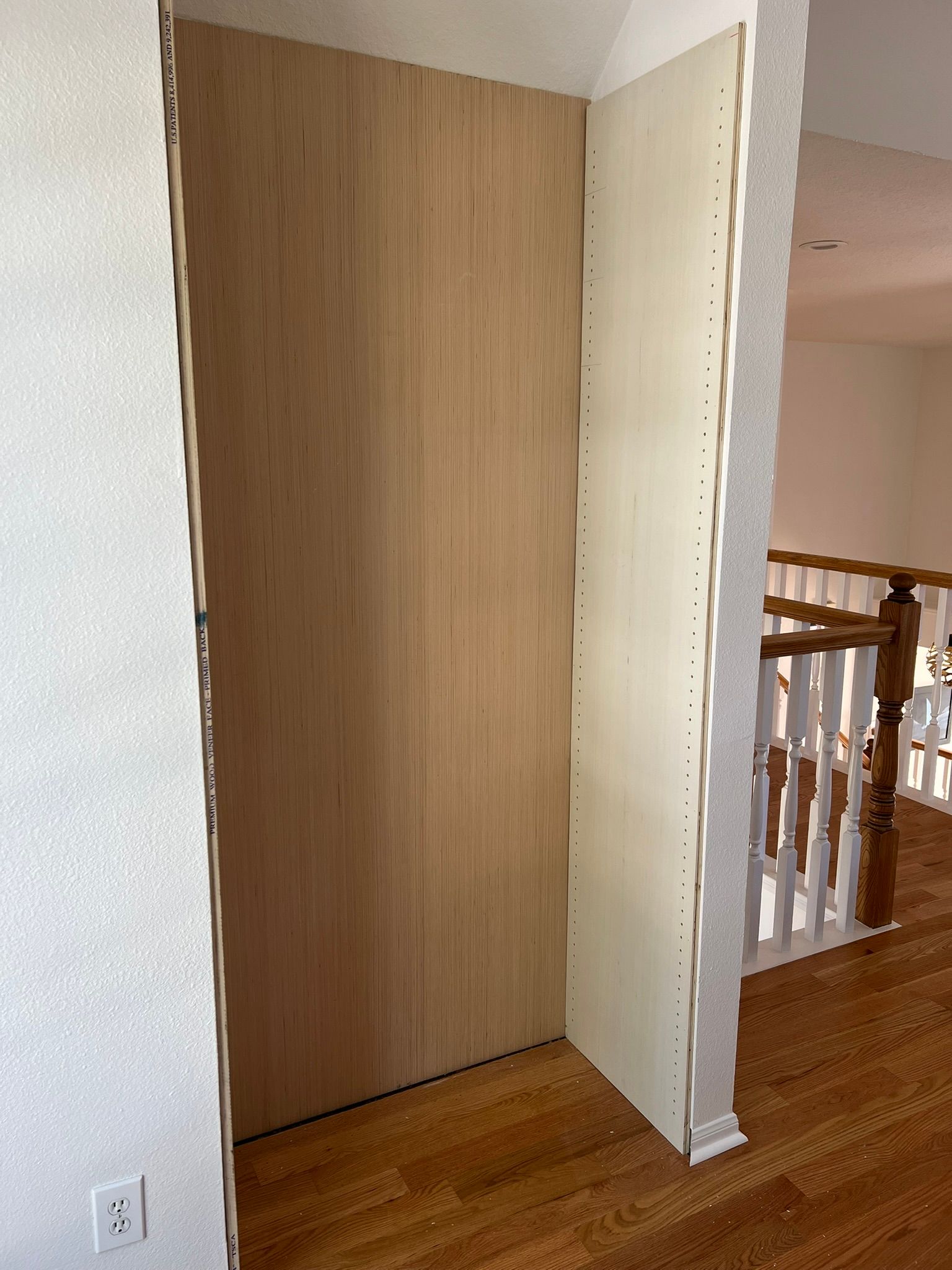 Closet opening with a wooden door panel and white wall beside a stair railing in a hallway.