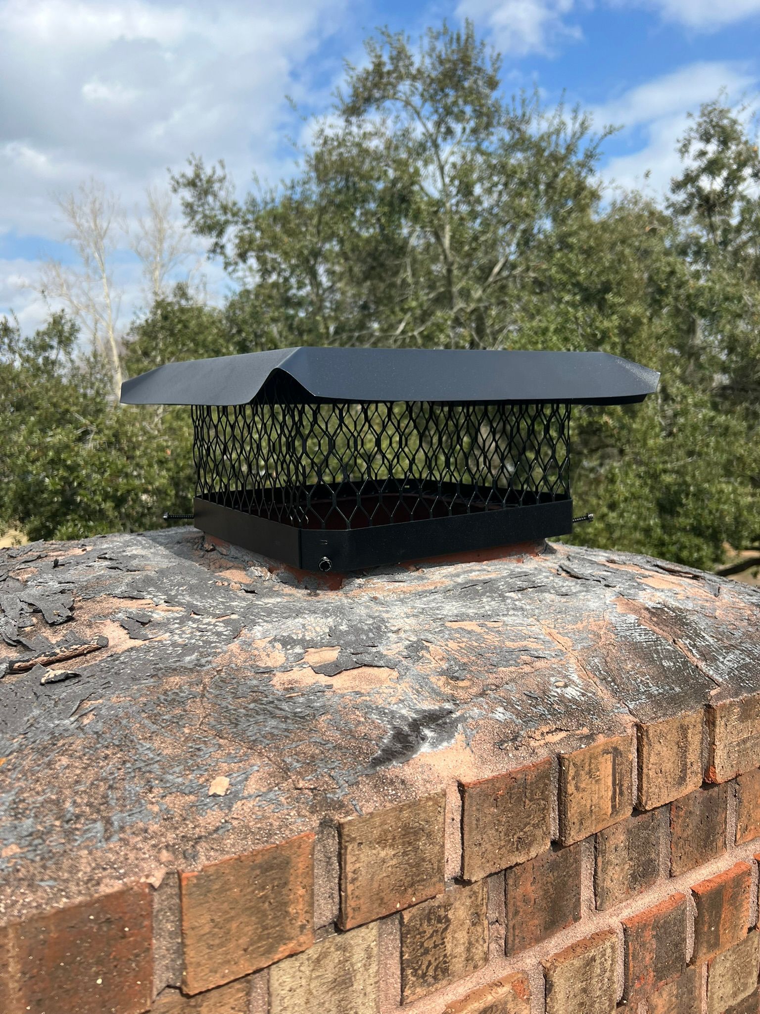 Black vent cap on a brick chimney against trees and cloudy sky