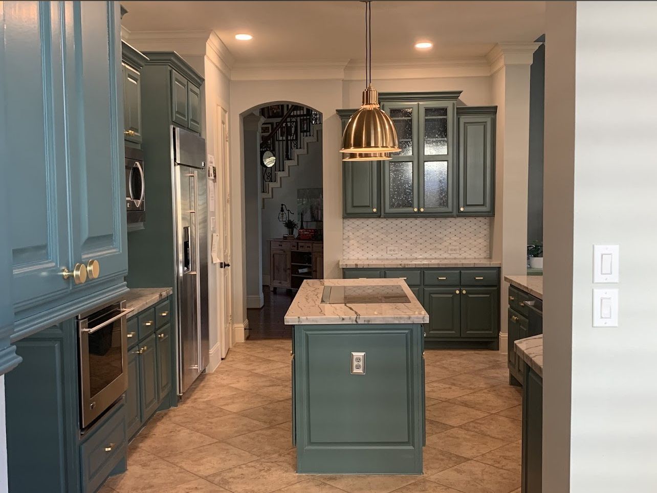 Blue-green kitchen with island, built-in oven, and pendant light in a bright, tiled interior